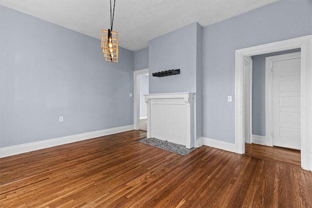 unfurnished living room with a chandelier, baseboards, and wood finished floors