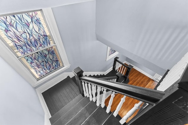 stairway featuring baseboards, a healthy amount of sunlight, and wood finished floors