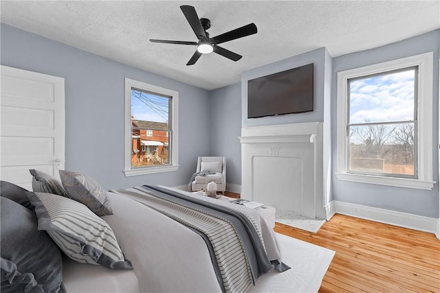 bedroom featuring baseboards, light wood-style floors, ceiling fan, and a textured ceiling