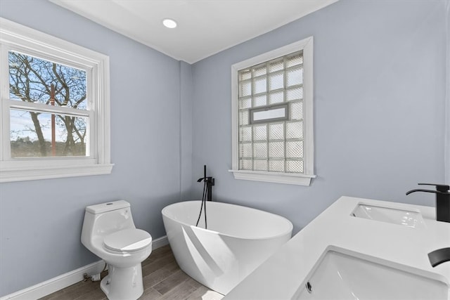 bathroom featuring dual sinks, baseboards, toilet, wood finished floors, and a soaking tub