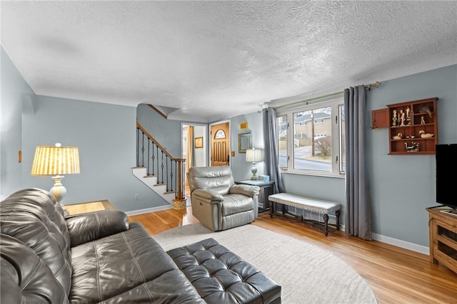 living area featuring stairway, a textured ceiling, baseboards, and wood finished floors