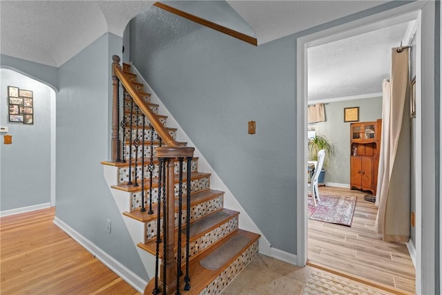 stairs featuring arched walkways, a textured ceiling, baseboards, and wood finished floors