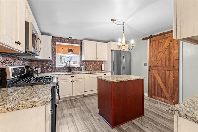 kitchen with light wood-type flooring, a sink, backsplash, stainless steel appliances, and a barn door