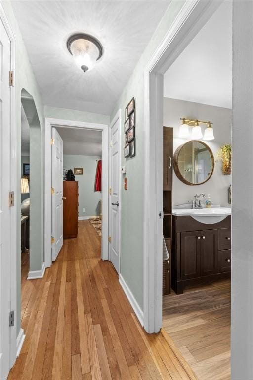 corridor featuring arched walkways, light wood-type flooring, baseboards, and a sink