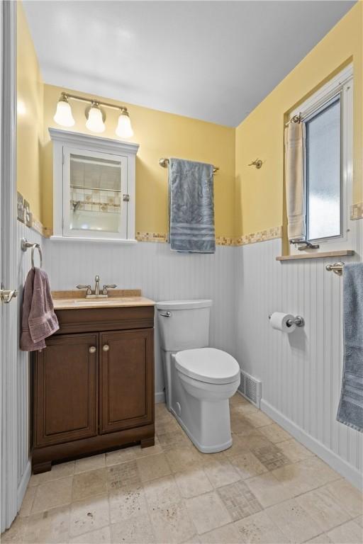 half bathroom with vanity, toilet, visible vents, and a wainscoted wall