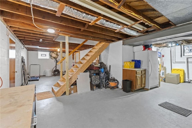 below grade area featuring stairway, concrete block wall, and freestanding refrigerator