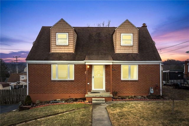 cape cod-style house featuring a front yard, fence, brick siding, and a chimney