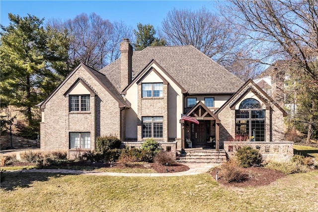 view of front of house featuring brick siding, a chimney, a front yard, and roof with shingles