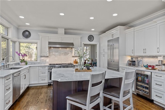 kitchen with beverage cooler, a sink, white cabinets, under cabinet range hood, and high quality appliances