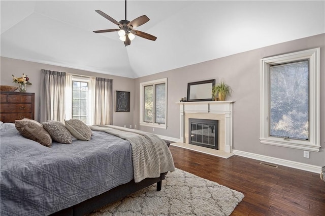 bedroom with visible vents, dark wood-type flooring, lofted ceiling, and a glass covered fireplace