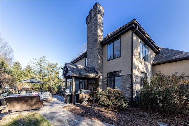 rear view of property with exterior kitchen, a shingled roof, stucco siding, a chimney, and a patio area