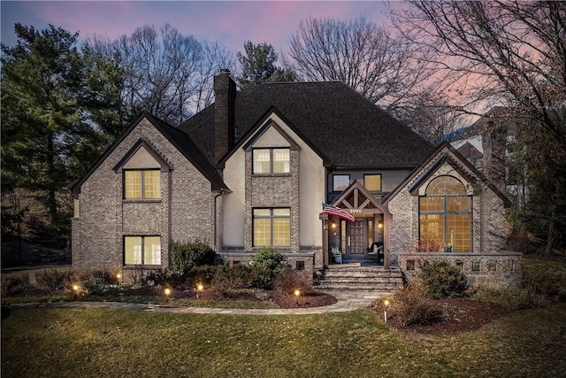 tudor home featuring brick siding, a lawn, a chimney, and a shingled roof