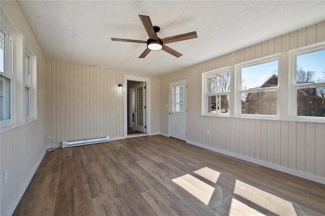 spare room with ceiling fan, a baseboard heating unit, baseboards, and wood finished floors