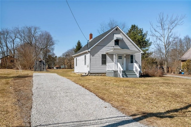 view of front of house with gravel driveway, a front lawn, and a chimney