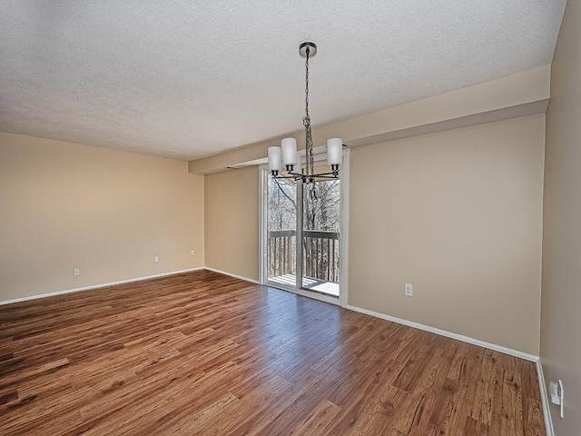 empty room featuring a textured ceiling, wood finished floors, baseboards, and a chandelier