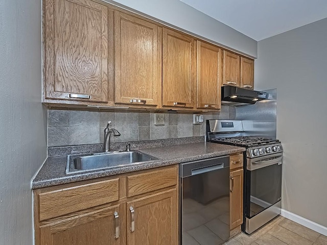 kitchen with dark countertops, under cabinet range hood, dishwasher, stainless steel gas stove, and a sink