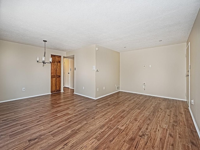 spare room featuring dark wood-style floors, baseboards, a textured ceiling, and an inviting chandelier