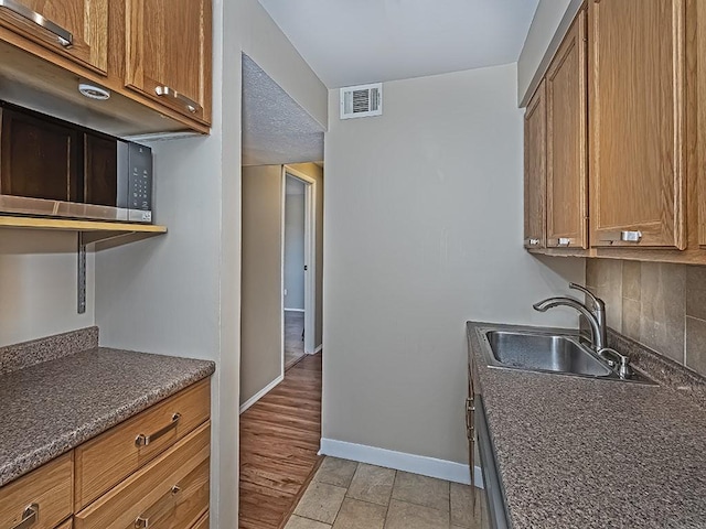 kitchen with visible vents, a sink, tasteful backsplash, brown cabinetry, and baseboards