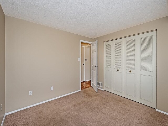 unfurnished bedroom featuring visible vents, a textured ceiling, a closet, carpet floors, and baseboards