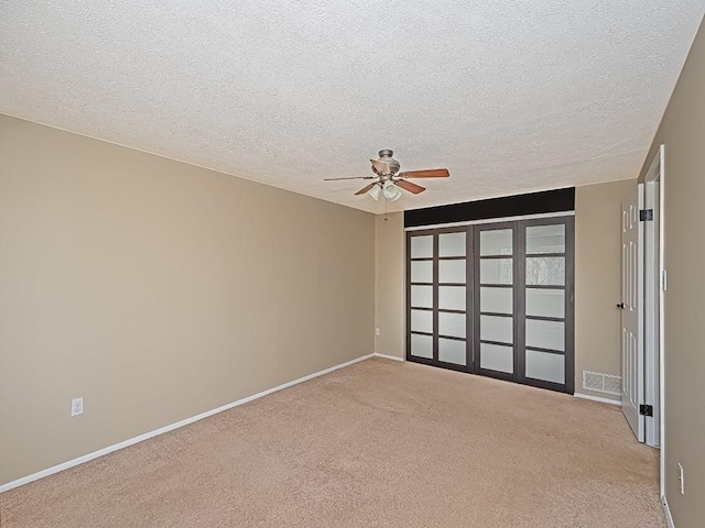 carpeted empty room with visible vents, baseboards, a textured ceiling, and a ceiling fan