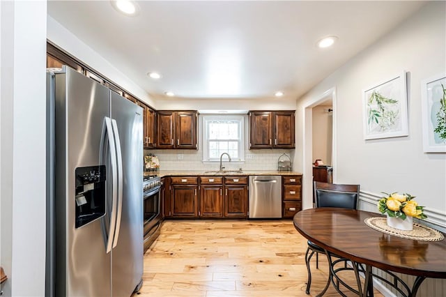 kitchen with light wood-type flooring, a sink, appliances with stainless steel finishes, decorative backsplash, and dark brown cabinets