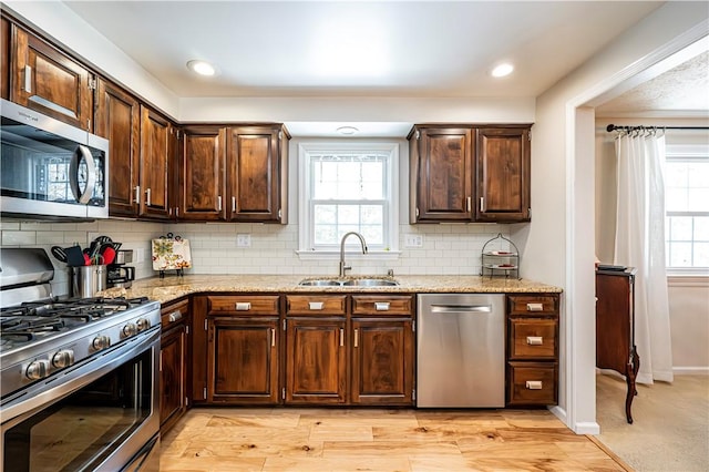 kitchen with light stone countertops, a sink, decorative backsplash, stainless steel appliances, and dark brown cabinets