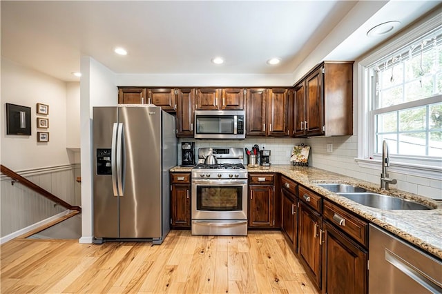 kitchen with light wood-type flooring, a sink, dark brown cabinetry, appliances with stainless steel finishes, and light stone countertops