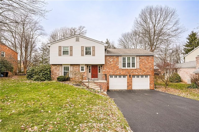 split level home featuring brick siding, an attached garage, aphalt driveway, and a front yard