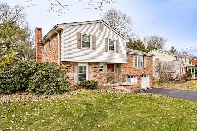 tri-level home with driveway, an attached garage, a front yard, brick siding, and a chimney