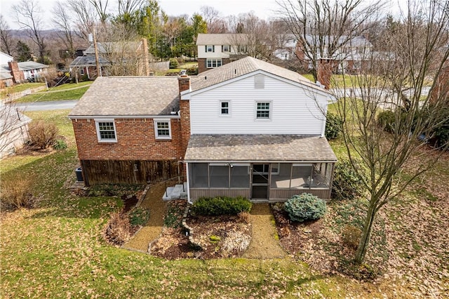 rear view of house with a sunroom, a yard, and roof with shingles