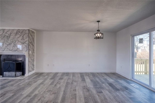 unfurnished living room featuring wood finished floors, visible vents, baseboards, an inviting chandelier, and a high end fireplace