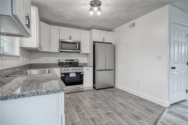 kitchen with wood finish floors, stainless steel appliances, visible vents, and white cabinetry