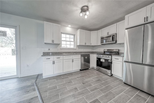 kitchen with white cabinetry, light stone counters, appliances with stainless steel finishes, and a sink