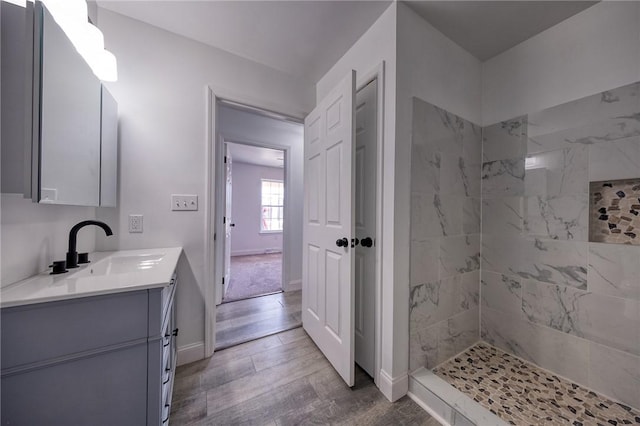 bathroom with baseboards, tiled shower, wood finished floors, and vanity