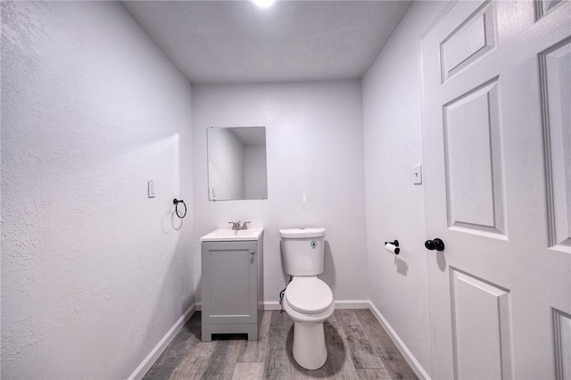 half bath with vanity, toilet, wood finished floors, and baseboards