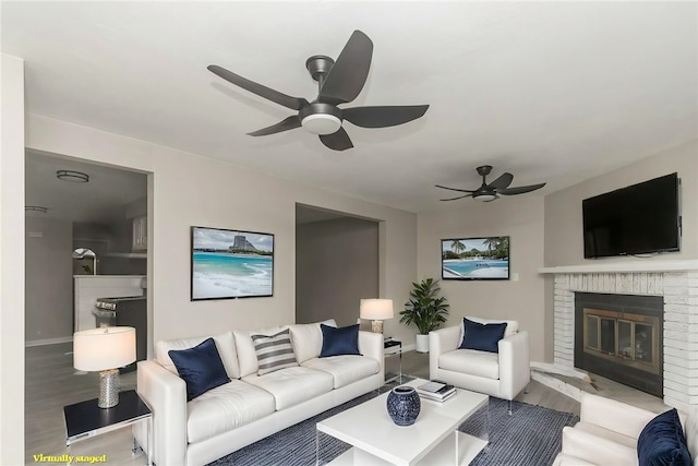 living area featuring ceiling fan, baseboards, a brick fireplace, and wood finished floors