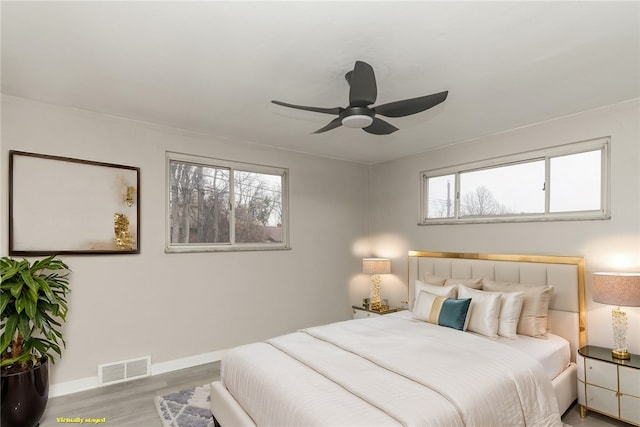 bedroom with a ceiling fan, wood finished floors, visible vents, and baseboards