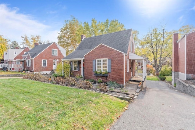 view of front of property with a shingled roof, a front yard, brick siding, and aphalt driveway