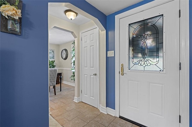 foyer with arched walkways and baseboards