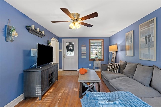 living room with arched walkways, light wood-style flooring, baseboards, and ceiling fan