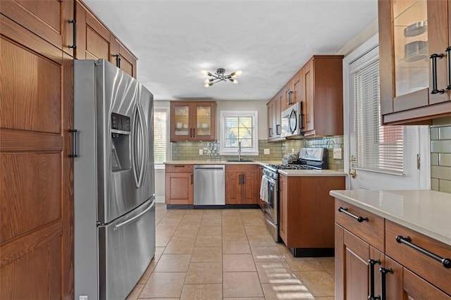 kitchen featuring backsplash, light countertops, brown cabinets, stainless steel appliances, and a sink