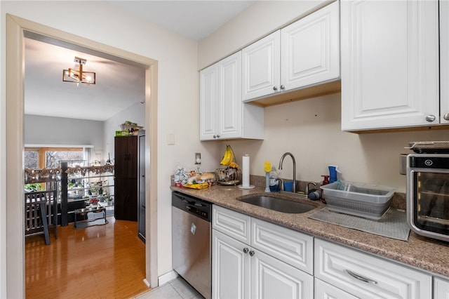 kitchen featuring a sink, light stone counters, stainless steel dishwasher, and white cabinetry