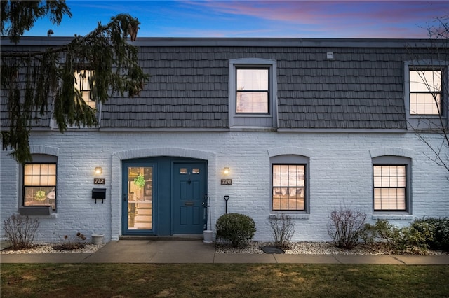 view of front of home featuring mansard roof and brick siding