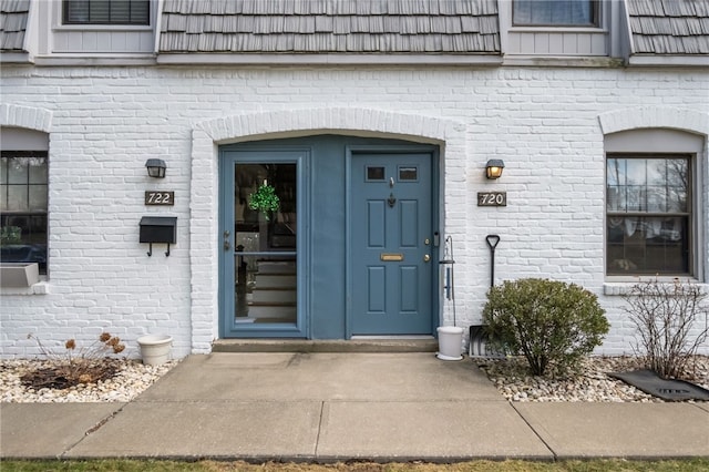 view of exterior entry featuring brick siding and mansard roof