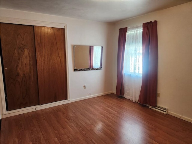 unfurnished bedroom with a closet, visible vents, baseboards, and wood finished floors