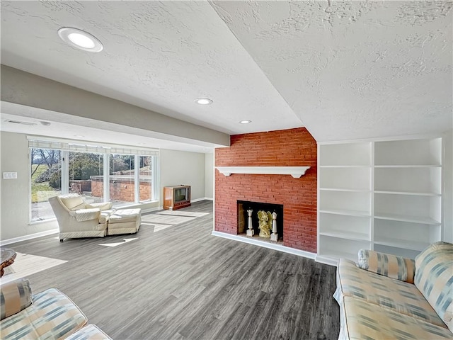 living room with a brick fireplace, a textured ceiling, baseboards, and wood finished floors