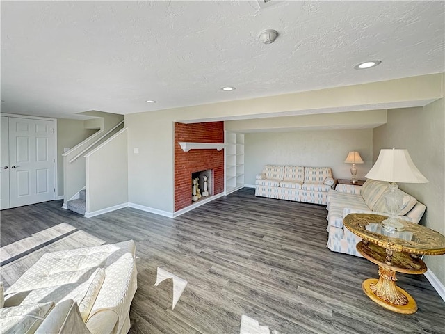 living area with stairway, wood finished floors, baseboards, a fireplace, and a textured ceiling