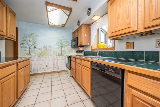 kitchen with baseboards, tile counters, light tile patterned floors, black appliances, and a sink