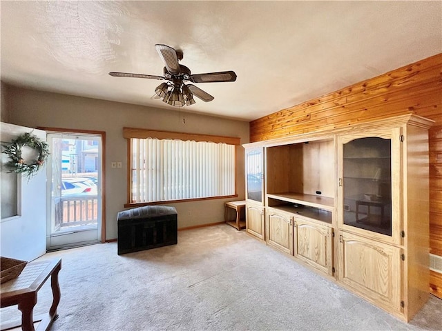 living area with light carpet, wooden walls, a textured ceiling, and ceiling fan