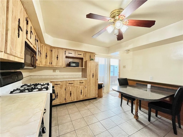 kitchen with ceiling fan, black microwave, light countertops, light tile patterned floors, and range with gas stovetop